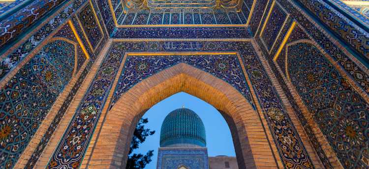 Ornate blue, gold and stone walls surrounding pointed archway | Samarkand, Uzbekistan